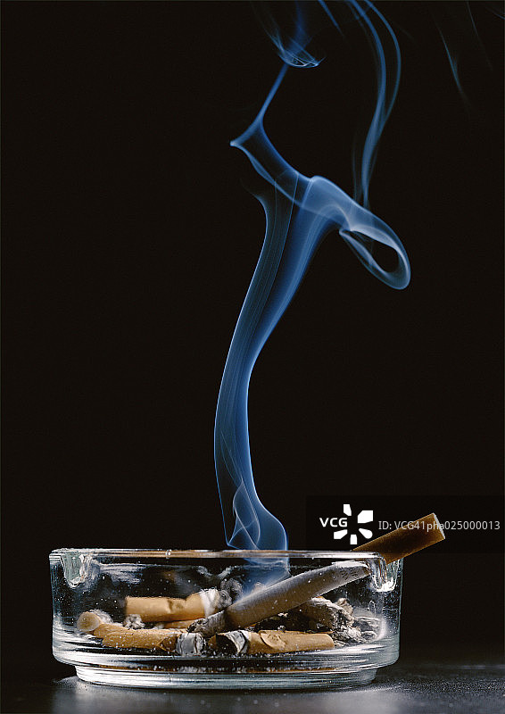 烟灰缸与烟头和点燃的香烟排放烟雾在黑色的背景图片素材