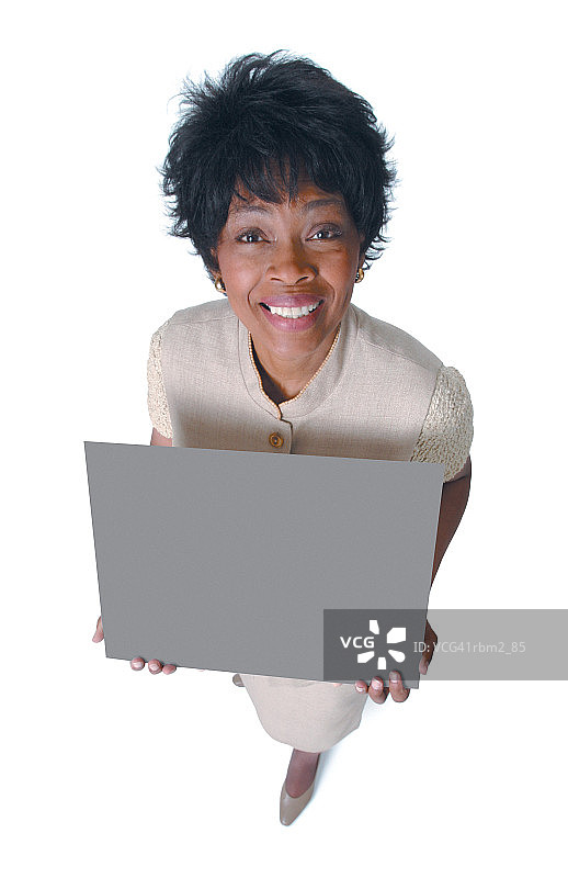 一位成年的非裔美国妇女穿着棕褐色的衣服，举着一个牌子，对着镜头微笑图片素材
