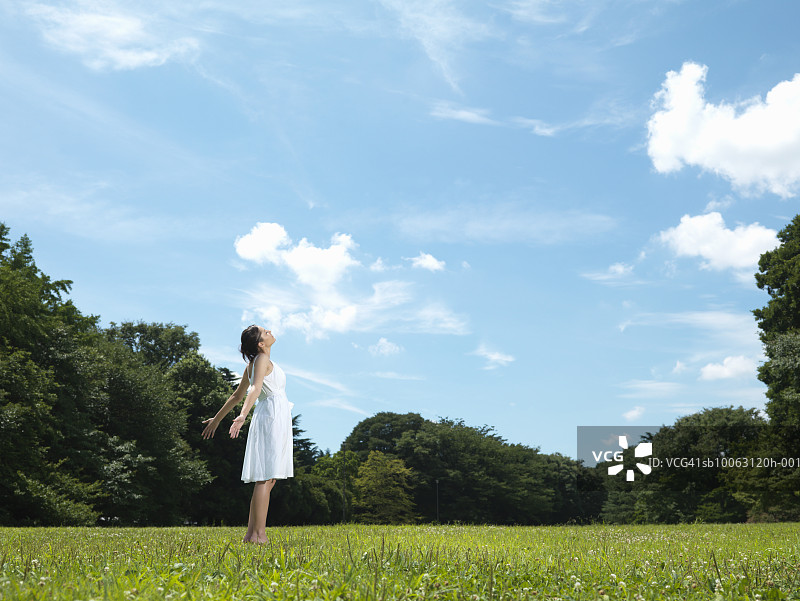 十几岁的女孩(16-17岁)站在草坪上，手臂伸出，侧视图片素材