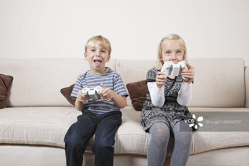 快乐的弟弟和妹妹在沙发上玩电子游戏图片素材