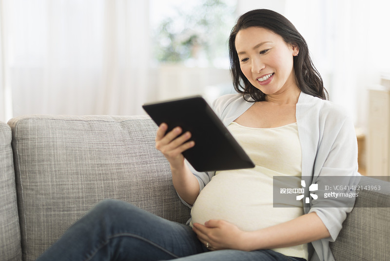 一名日本孕妇在沙发上使用平板电脑图片素材
