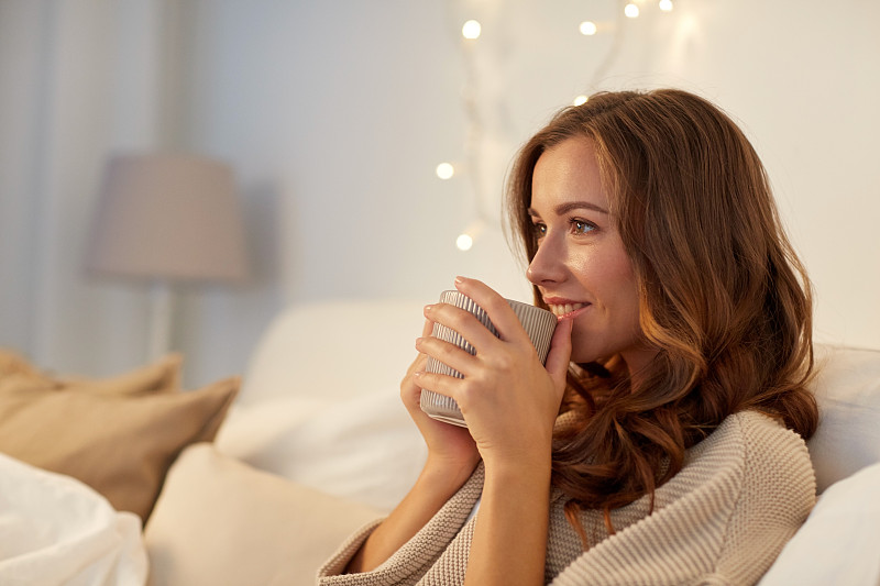 冬季，休闲与人的理念——幸福年轻女子在家中卧室的床上喝一杯咖啡或茶图片素材