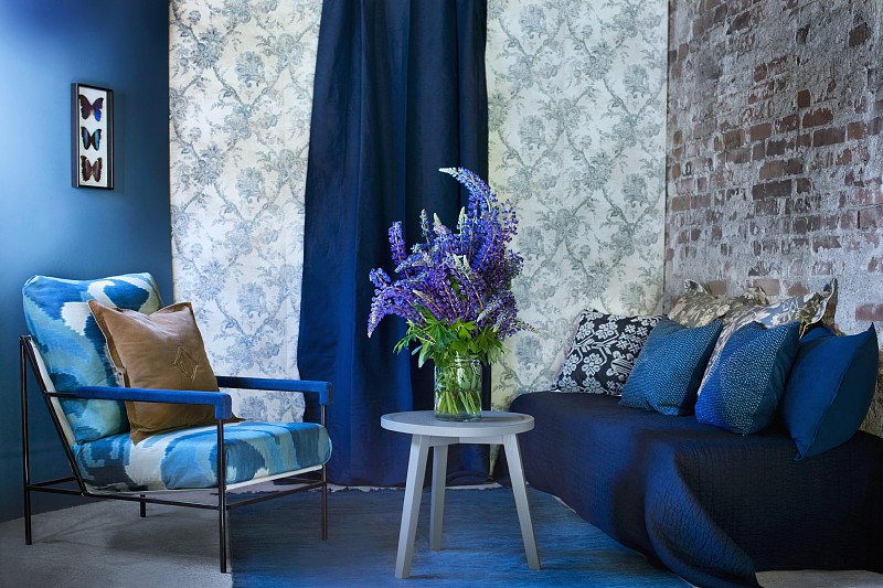 蓝色的墙面，有图案的墙纸和砖墙作为背景，蓝色的休息区配有沙发、扶手椅和一束羽扇花图片下载