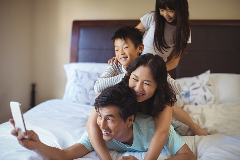 幸福的家庭在家里的卧室里用手机自拍图片下载
