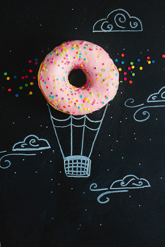 粉色的甜甜圈和粉笔画的热气球。创造性的概念。低调的食物摄影。图片素材
