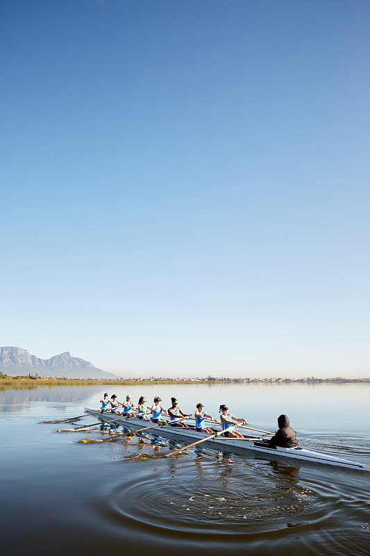 蓝天下，女子桨手在宁静的湖面上划桨图片下载