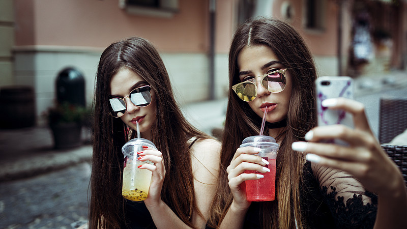 两个年轻的女人戴着太阳镜在城市街道上自拍图片素材