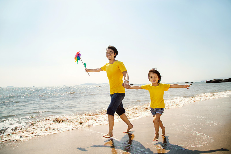 年轻父亲和女儿拿着风车在沙滩上奔跑图片下载