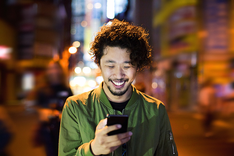 快乐的日本年轻人在晚上使用智能手机，东京。图片下载