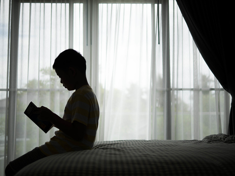 男孩坐在床上看书的侧视图图片素材
