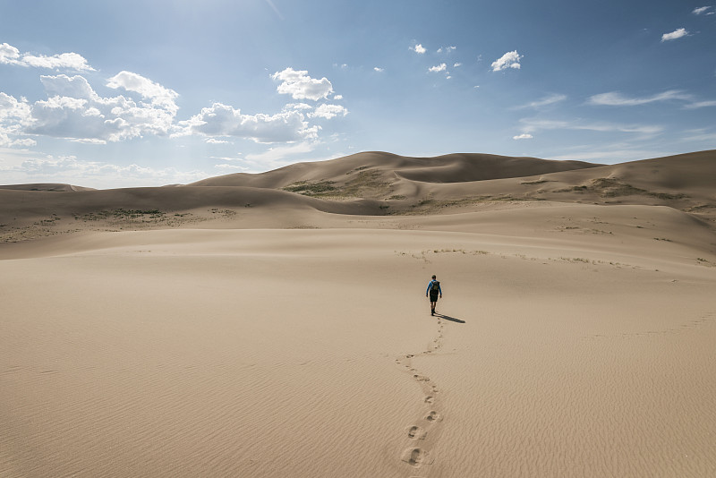 徒步者在大沙丘国家公园的天空下行走在沙漠上的后视图图片下载