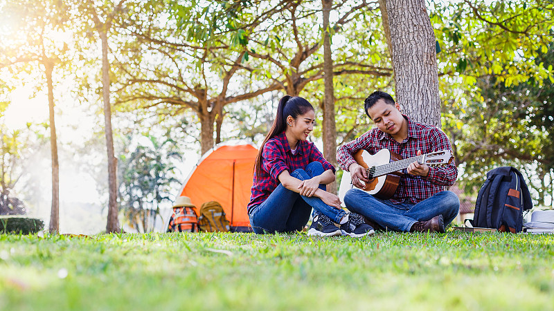 年轻的夫妇露营享受弹吉他和坐在户外露营帐篷，夫妇露营的概念图片素材