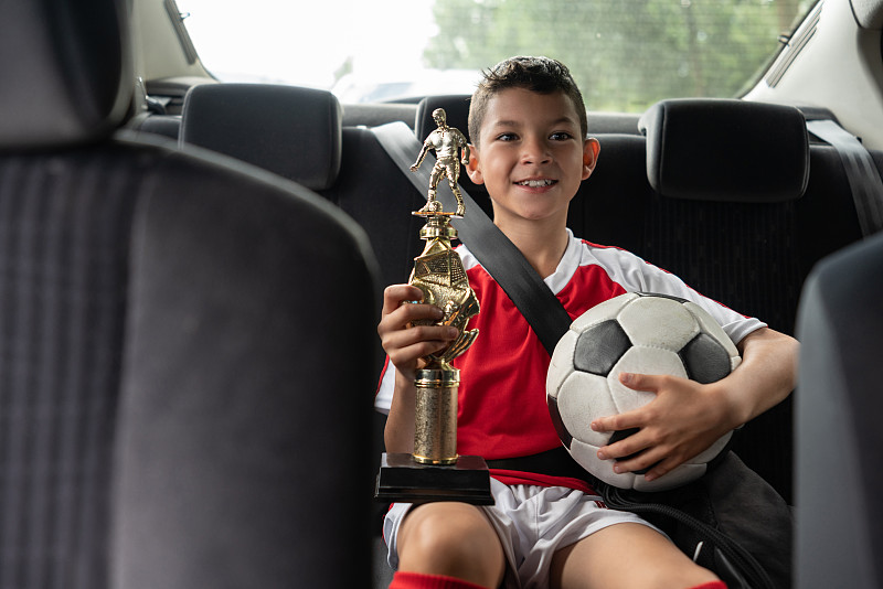 男孩在车后足球训练显示，高兴地拿着奖杯图片下载