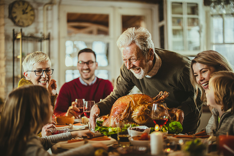 快乐的老人在餐桌上为家人烹制感恩节火鸡。图片下载