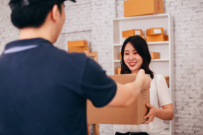 快乐的亚洲成年商业女性在办公室收到一个包裹从男性快递员图片下载