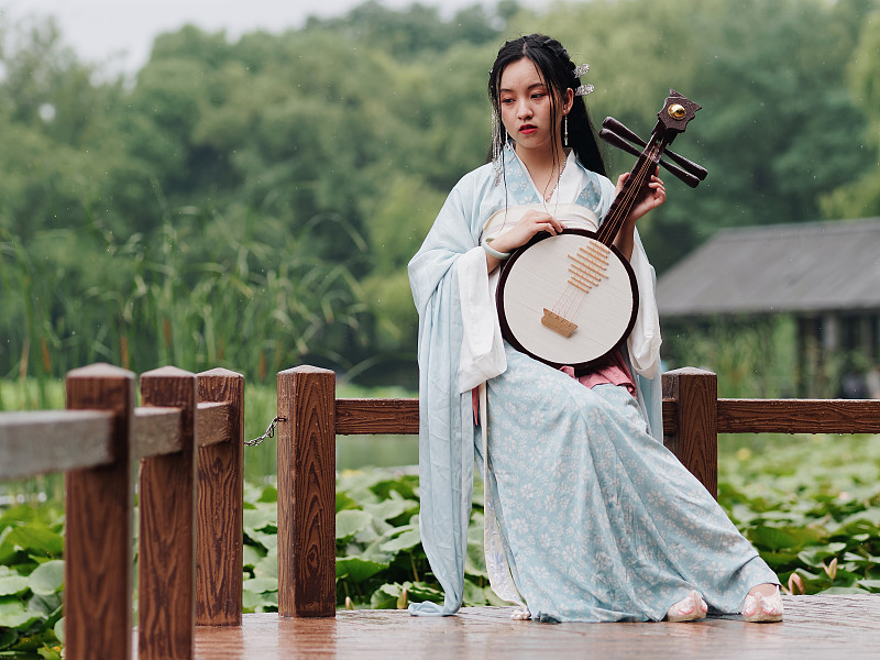 美丽的亚洲女人在青色服装汉服拿着月琴(四弦乐器)与荷塘背景在雨天，传统的中国古代美丽，时间旅行小说。图片素材