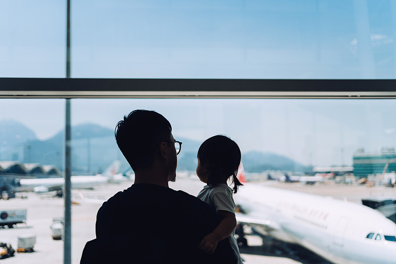 在机场等待起飞的时候，快乐的年轻亚洲父亲抱着可爱的小女儿，透过窗户看着飞机的剪影图片下载
