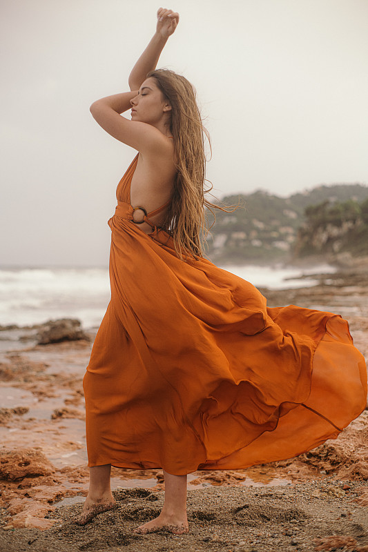 性感的女人在沙滩上摆姿势在橙色的裙子图片下载