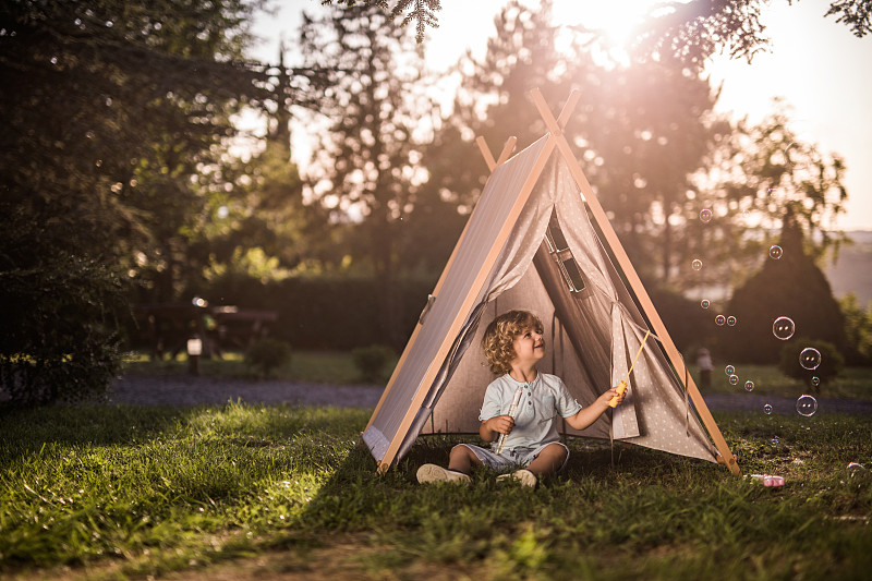 一个快乐的小男孩在帐篷里玩泡泡棒。图片下载