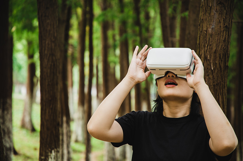 一个女人在森林中使用虚拟现实头盔图片下载