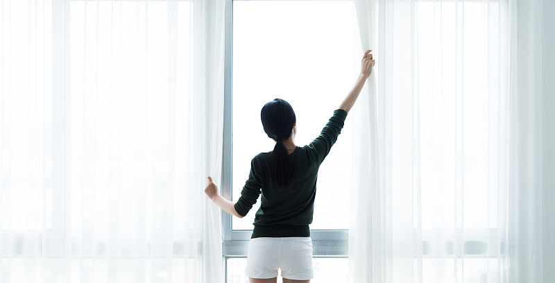 一位亚洲妇女拉开窗帘，望向窗外图片下载