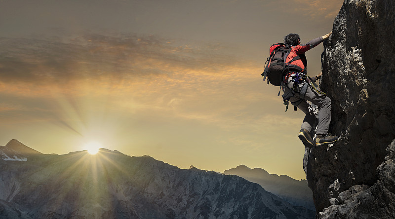 日落时分，一名登山者站在岩壁上图片下载