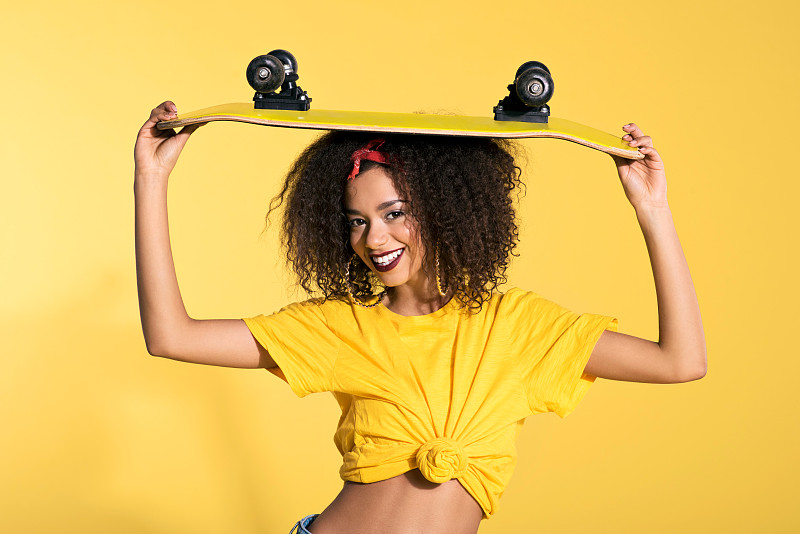 快乐的年轻黑人妇女拿着滑板在她的头上图片下载