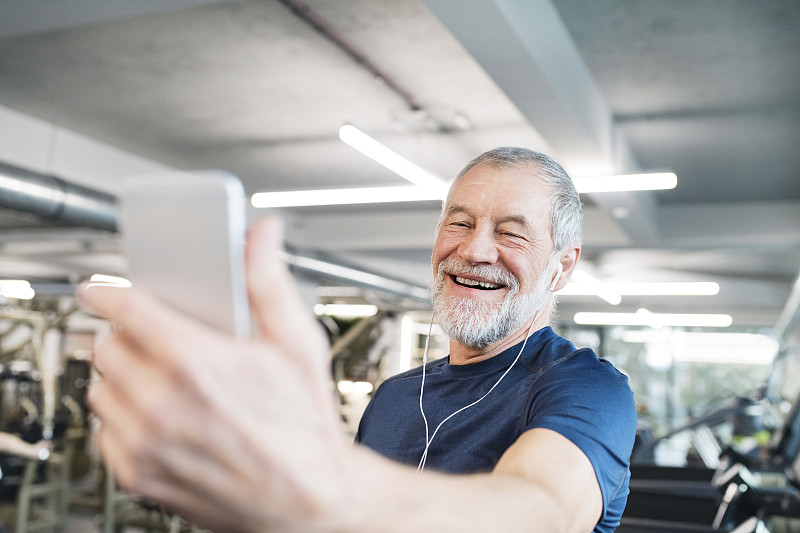 在健身房里，带着智能手机和耳机的快乐老人图片下载
