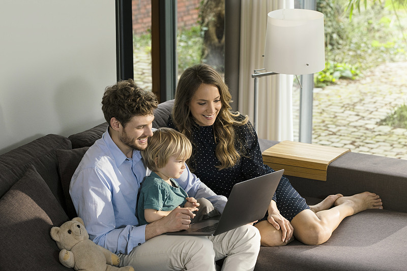 微笑的父母和儿子坐在沙发上使用笔记本电脑图片下载