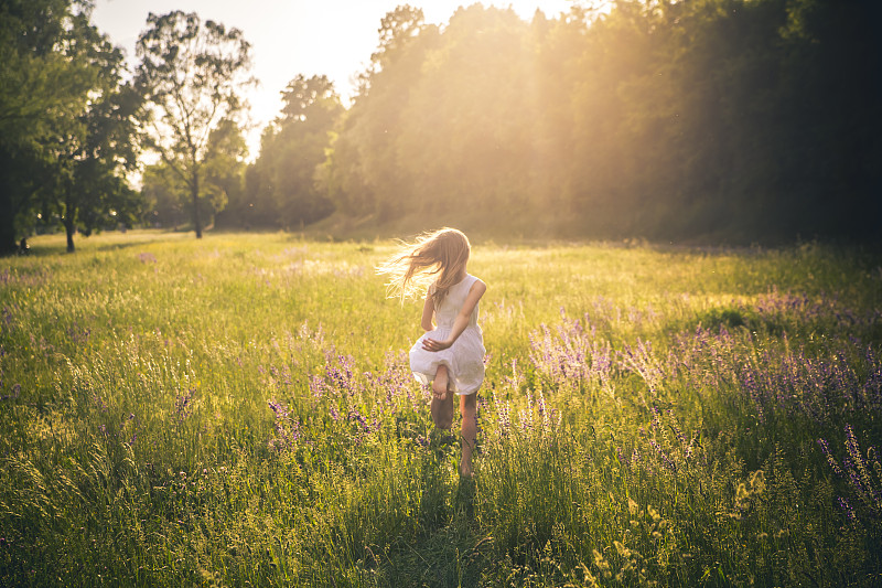 黄昏时分，女孩在花草地上奔跑的背影图片下载