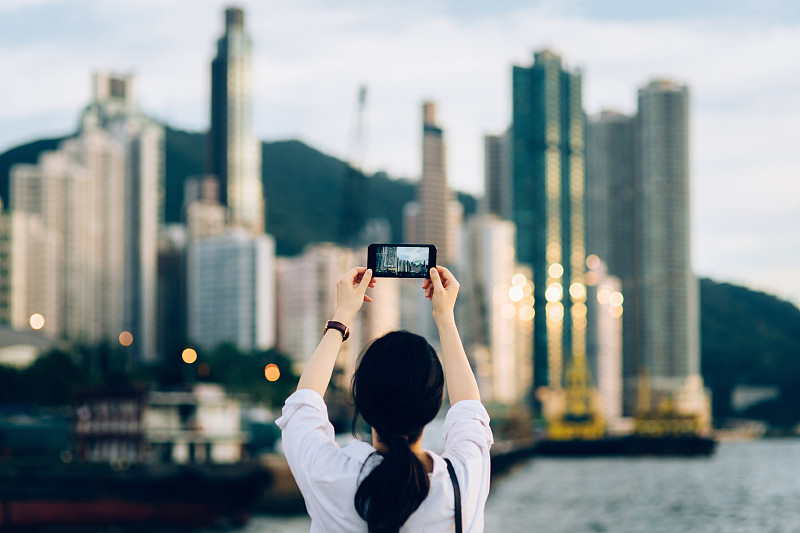 年轻女子在日落时用手机拍摄美丽的城市天际线图片素材