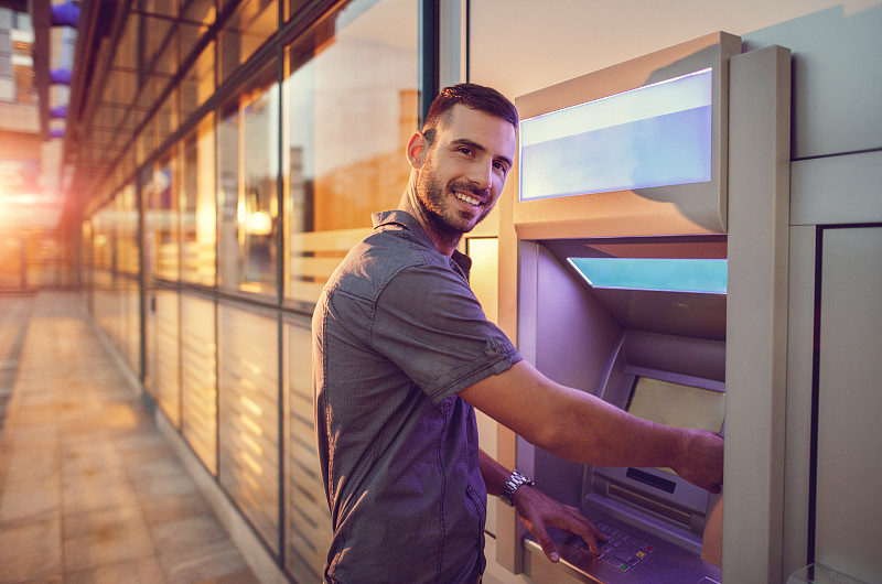 微笑的年轻商人从ATM机取款。图片素材