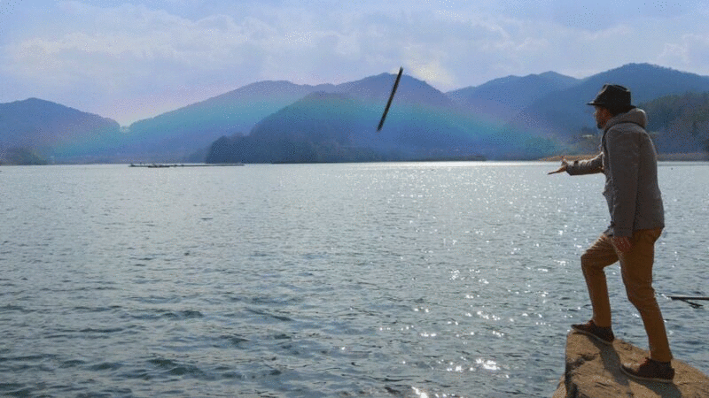 一名男子向湖边的彩虹投掷木棍图片下载
