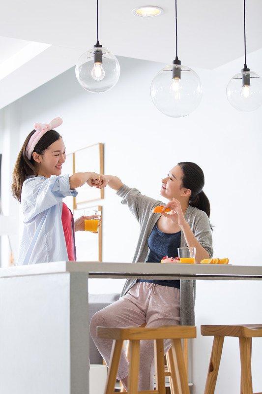 两个青年女子在起居室吧台吃橙子喝果汁顶拳聊天嬉戏图片下载