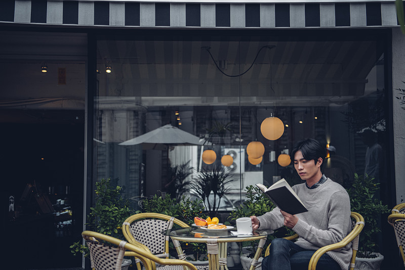 男子坐在桌子旁喝咖啡看书的照片在café户外摄影图片下载