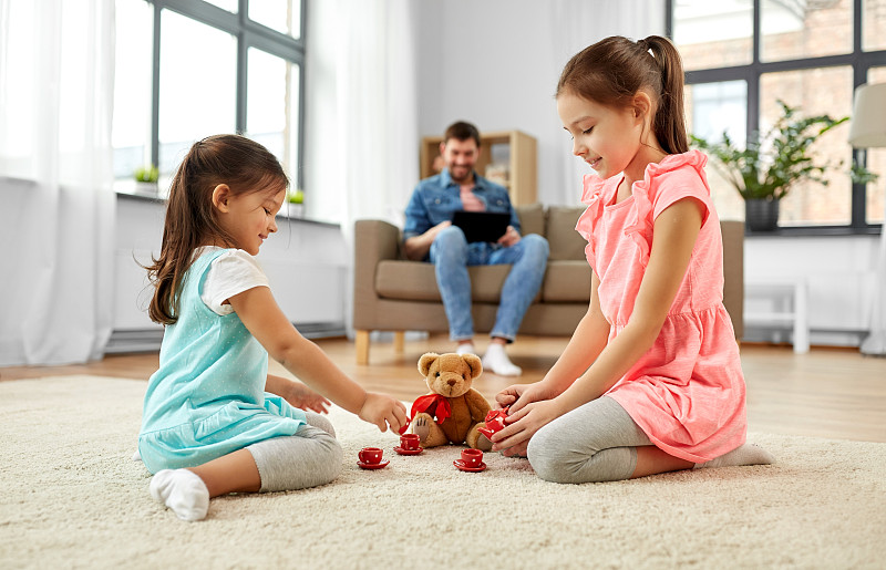童年，休闲和家庭概念-小姐妹们在家里玩茶会游戏，玩具陶器和泰迪熊。女孩们在家里玩玩具陶器和泰迪熊图片下载
