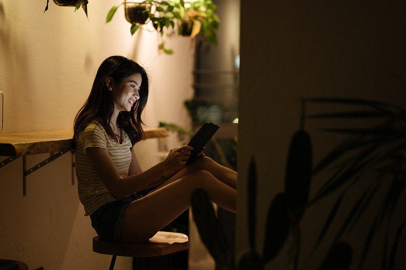 亚洲年轻女孩夜晚在家使用平板电脑图片素材