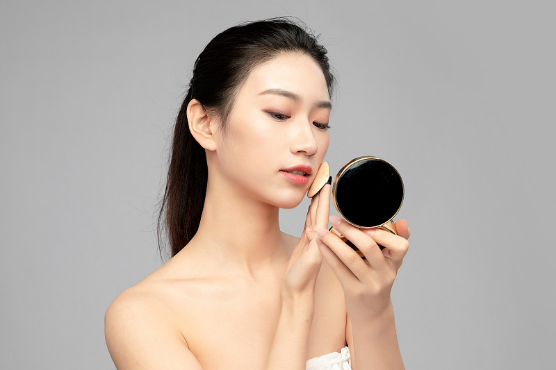 灰色背景里正在使用粉饼的亚洲美女面部特写，化妆护肤整容图片素材