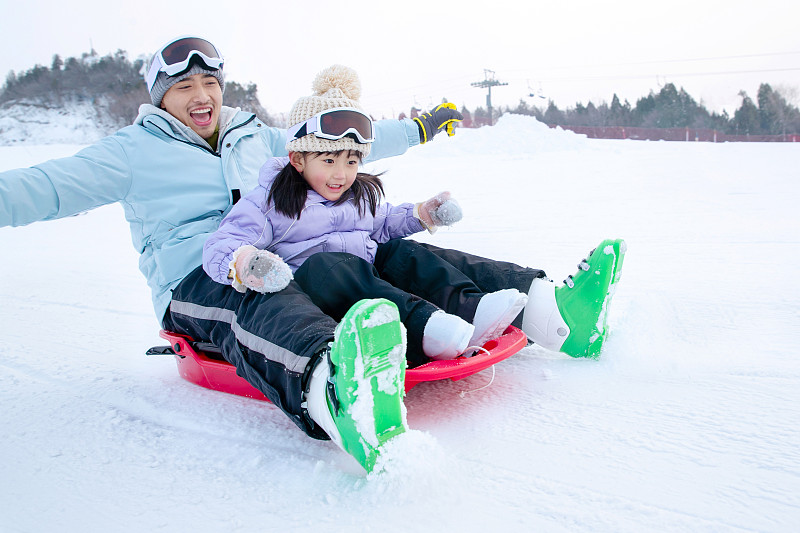 滑雪场上快乐父女坐着雪上滑板滑雪图片下载