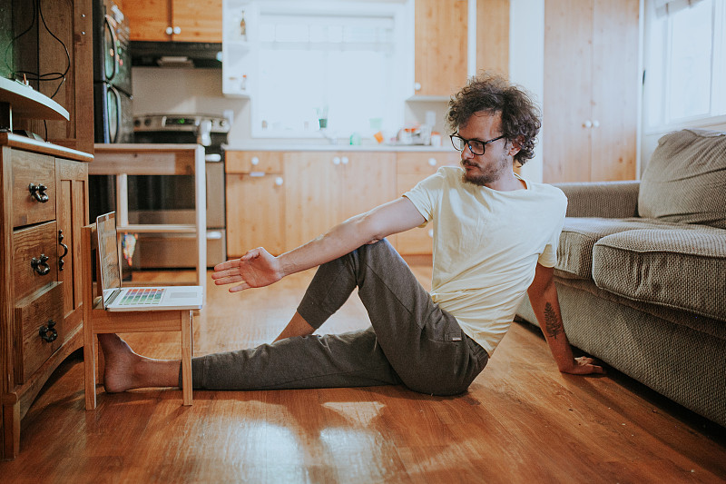加拿大维多利亚，一名男子一边看笔记本电脑一边在地板上做伸展运动图片下载