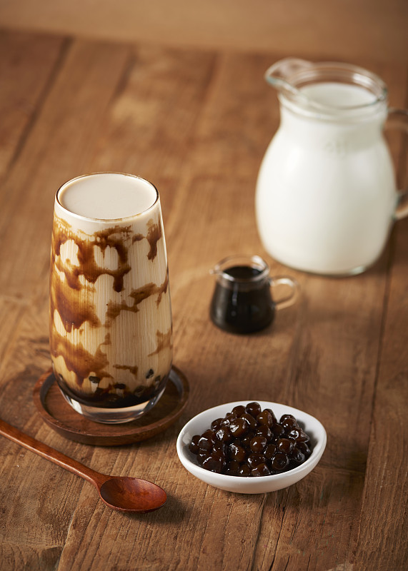 红糖奶茶旁边的牛奶，酱汁，木薯珍珠和勺子放在木地板上图片下载