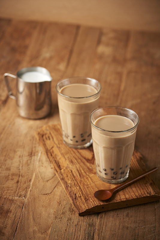 木制托盘上放着两杯带珍珠粉的棕色奶茶，牛奶旁边放着勺子图片素材
