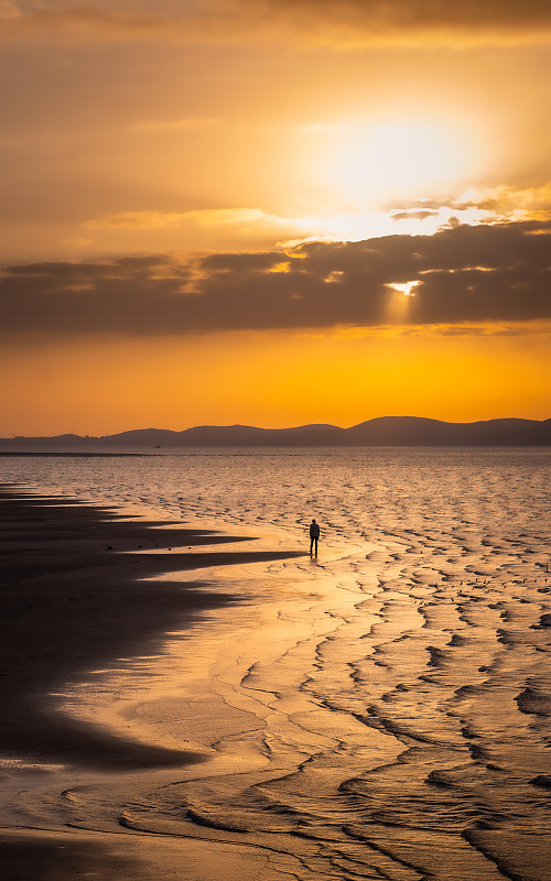 黄昏夕阳西下时，一个人独自在海边沙滩上徘徊的孤独背影图片下载