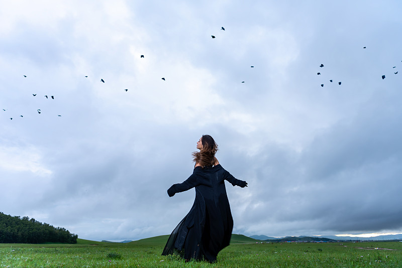 夏天草原上一个穿黑色连衣裙自由奔跑的东方年轻女性图片下载