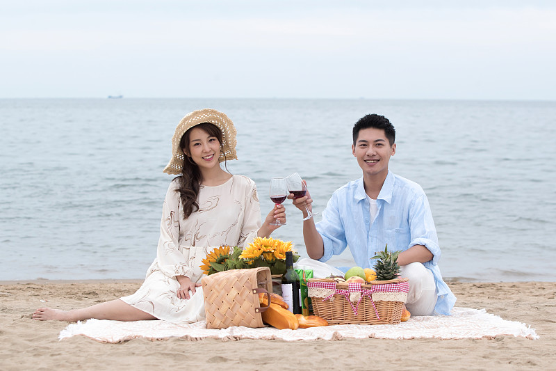 浪漫的青年夫妇坐在沙滩上喝红酒图片素材