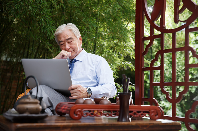 一个商务老年男人坐在院子里使用电脑图片下载