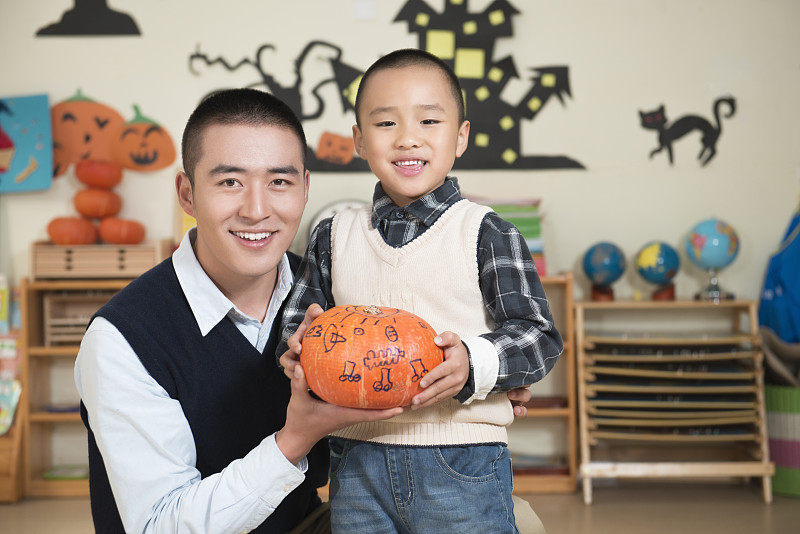Kindergarten teacher and boy carving pumpkin图片下载