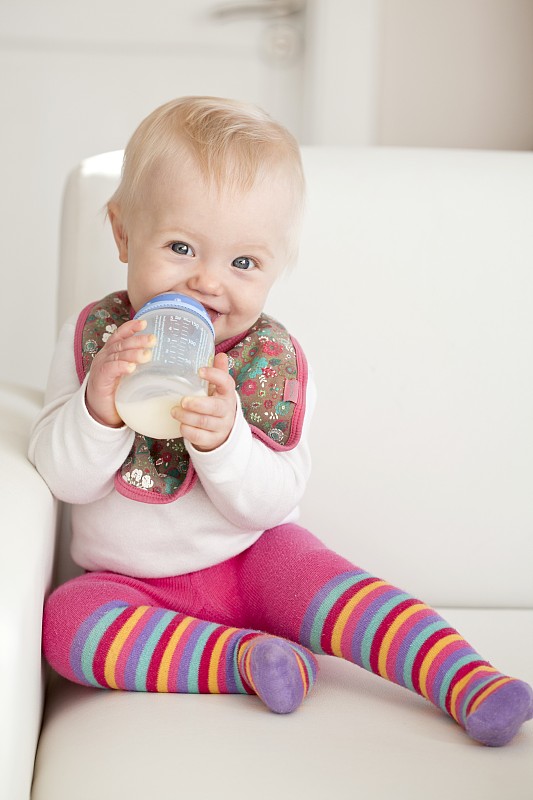 一个婴儿坐在沙发上，手里拿着一瓶牛奶图片下载