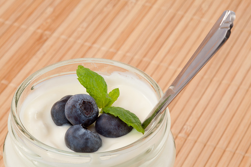 特写:四个蓝莓放在一个用勺子舀的酸奶里图片下载