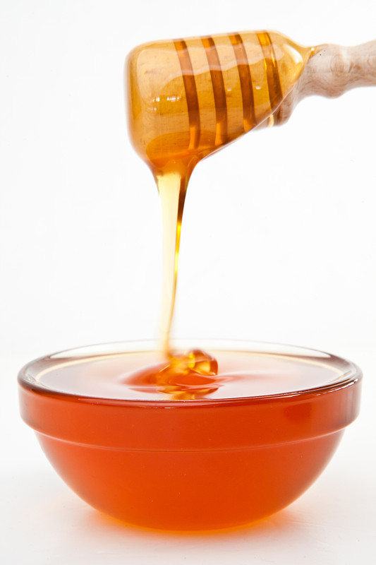 在白色的背景下，蜂蜜在蜂蜜勺上掉落在碗里图片下载